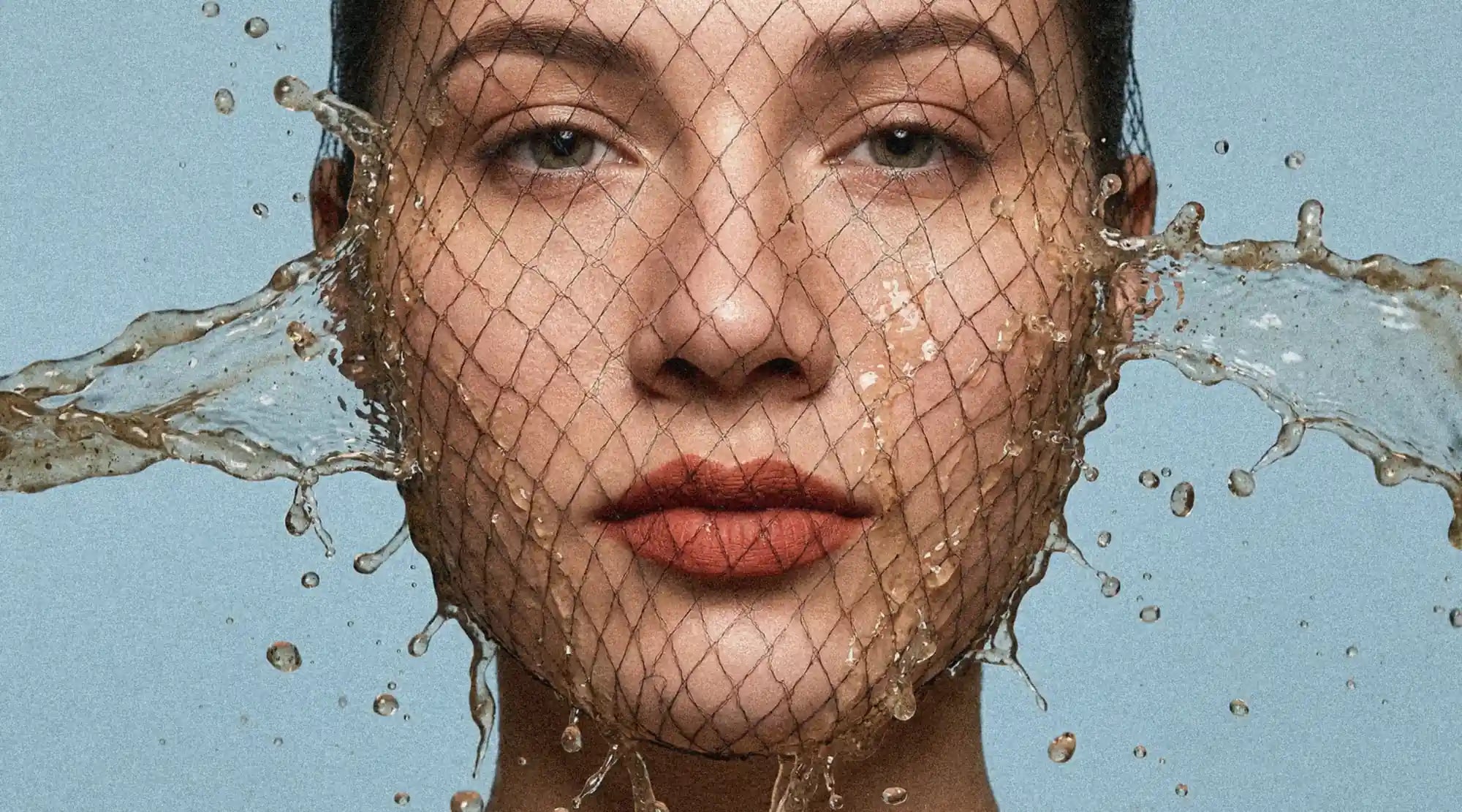 A face of a woman in a fishnet splashed by water